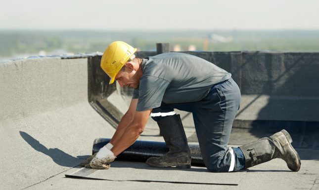 Roofer Preparing Part of Bitumen Roofing Felt Roll for Melting by Gas Heater Torch Flame